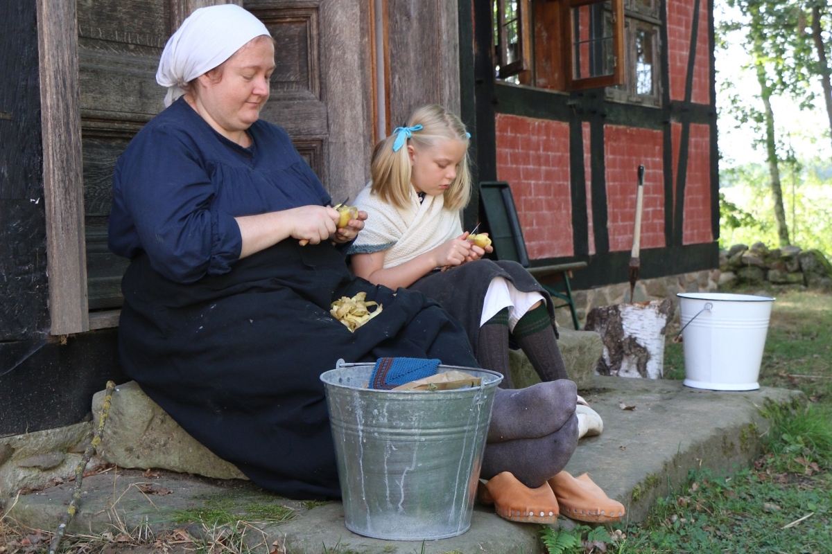 Frau und Kind in historischer Kleidung schälen Kartoffeln